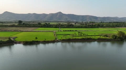 Drone flying parallel to river with farmland road and mountains at sunset 스톡 동영상 336972014