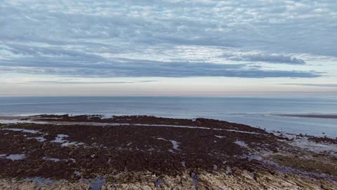 Drone flying from rocky beach to tranquil ocean under dramatic cloudy sky Stock Footage 309764156