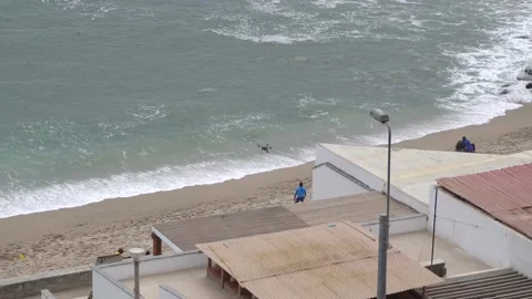 A drone flying on the shore of a beach between people and the waves of the sea Vidéo 181893775
