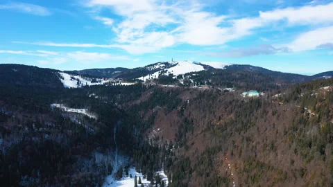 Drone flying sideways over forested mountain valley with snow patches Video stock 332047842