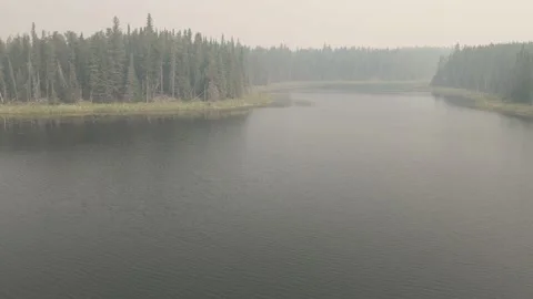 Drone flying slowly forward and rising over a small lake that is covered smoke Stock Footage 158453568
