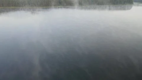 Drone flying slowly forward over a calm northern lake as mist rises from the Stock Footage 326831151