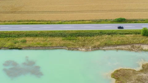 Drone flying slowly sideways over small pond and a corn field split by a road Video stock 305564691