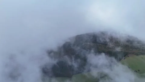 Drone flying through low clouds over green mountain hillside Stock Footage 332567155