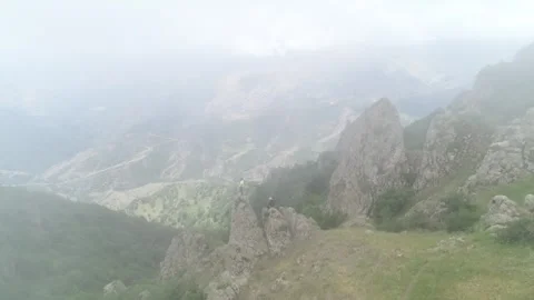 Drone Flying Through Mist Toward Tourists Sitting on Mountain Rocks 動画素材 311665778