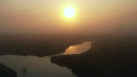 Drone flying through thick fog over mysterious field and winding river, rising Stock Footage 153931889
