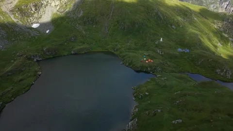 Drone flying toward alpine lake with tents and visitors in Făgăraș Mountains Stock Footage 340824387