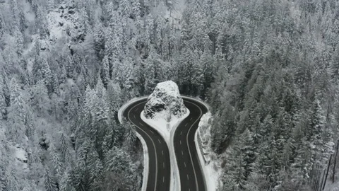Drone flying towards winding mountain road curve around rock in snowy forest Video stock 331986135
