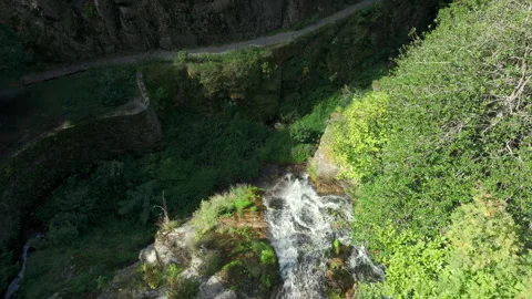 Drone flyover above a waterfall crest moving towards a rocky ravine with a stone Stock Footage 333050630