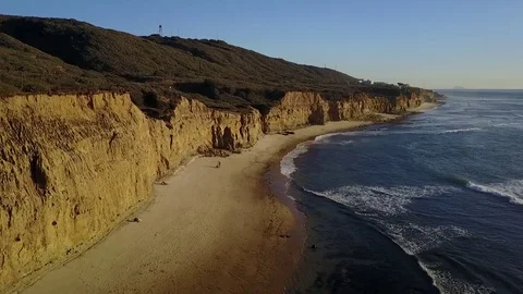Drone flys over beach with cliffs and ocean in frame during golden hour 스톡 동영상 71132459