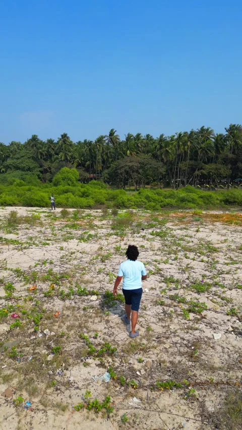 Drone Following Boy Across Sandy Terrain Toward Coconut Grove at Shirgaon Beach 動画素材 336799593