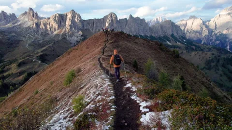 Drone follows back view of hiker walking with trekking poles along narrow snowy Stock Footage 346768926