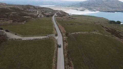 A drone follows a car driving down the road along the Barley Cove beach in Mizen Stock Footage 233196478