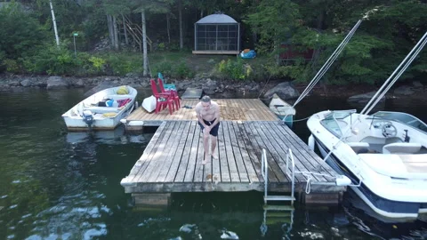 Drone follows in front of man taking running dive off cottage dock Stock Footage 231001716