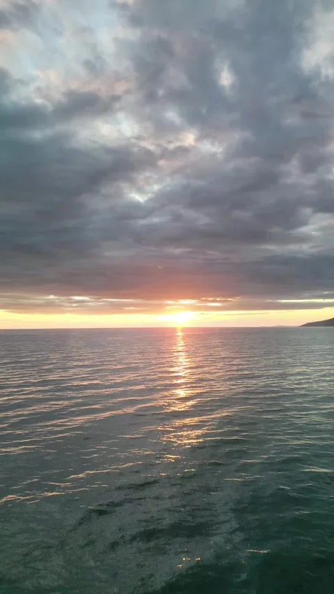 Drone follows the sun's rays over the wavy, clear sea and the sunset Video stock 312450254