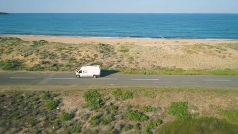 Drone follows white van or minibus driving along coastal road next to sand beach Stock Footage 134674500