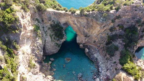 Drone footage of arch in rock formations set against a clear blue water sea Stock Footage 234857695