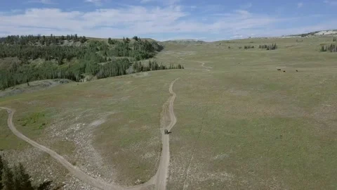 Drone footage of an ATV driving down a dirt road through a mountain valley Stock Footage 132229055