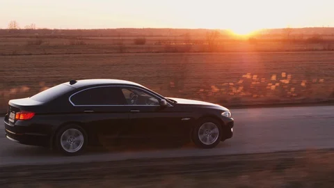 Drone footage of bmw black car driving on the road. Sun rays on horizon. Saint P Stock Footage