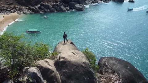 Drone Footage of Boy Standing Still on Rock with Sea and Mountains Ahead Stock Footage 284375802