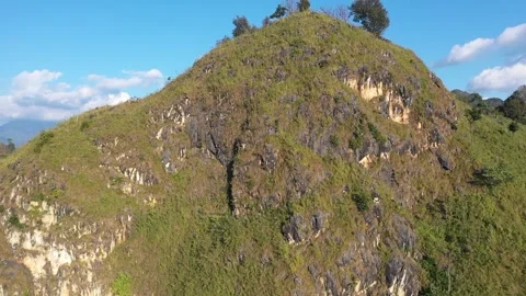Drone footage capturing a rugged, grassy mountain peak with scattered trees and Stock Footage 346665307