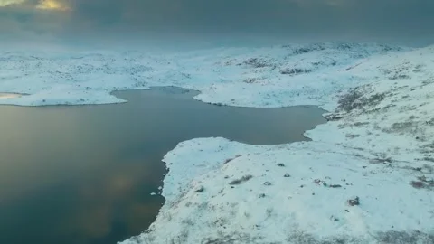 Drone footage capturing a snow-covered landscape featuring a serene lake surroun Stock Footage 308951862