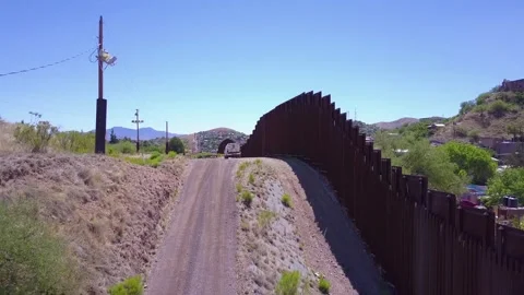 Drone footage flies along border wall toward town with houses on hills. Stock Footage 337761099