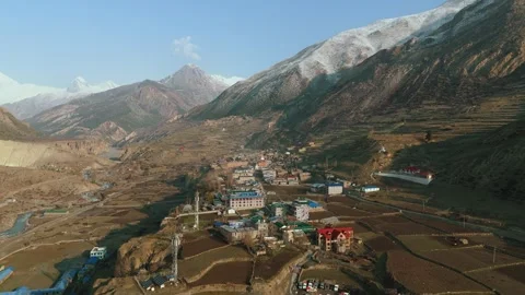 Drone footage of Manang’s traditional rooftops framed by towering white peaks. Stock Footage 311018714