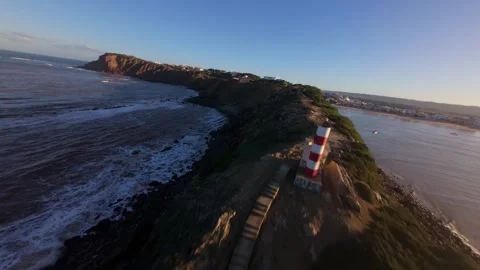 Drone footage shows dramatic sea cliffs, foamy surf, and distant lighthouse Stock Footage 344581986