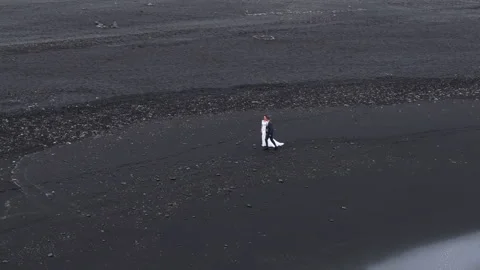 Drone footage of tiny silhouettes of bride and groom on Reynisfjara beach Stock Footage 259786148