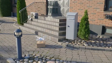 Drone in front of a house pick up package and fly away Stock Footage 82432429