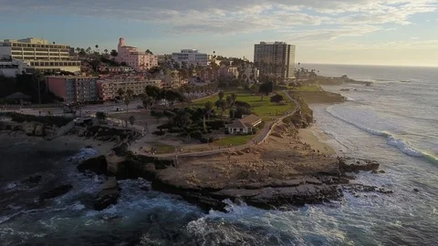Drone glides backwards along La Jolla cove showing seal lions, tourists 50' Stock Footage 95865594