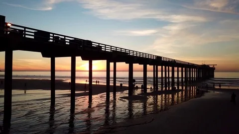 Drone glides FAST 10 feet over beach to water sunset seen through pier pillars Stock Footage 85454073
