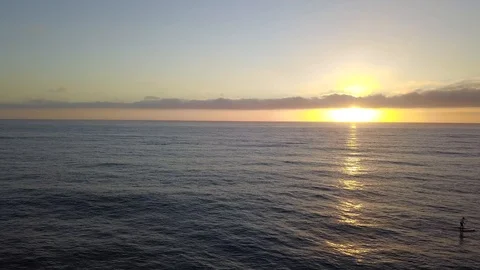 Drone glides over ocean passing a SUP Stand Up Paddleboarder at sunset Stock Footage 95063393
