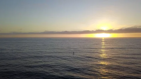 Drone glides over ocean toward setting sun passing a SUP Stand Up Paddleboarder Stock Footage 95063229