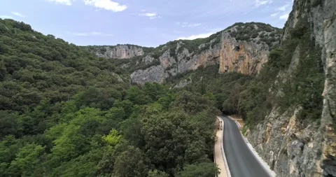 Drone glides over a winding road in Ardèche, France, with forests and cliffs Stock Footage 290959038