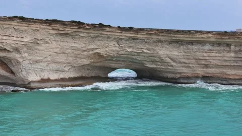 Drone glides toward sea arch in limestone cliffs malta coastline turquoise cove Stock Footage 343571931