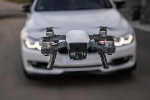 Drone hovering in front of a luxury white car Stock Photos