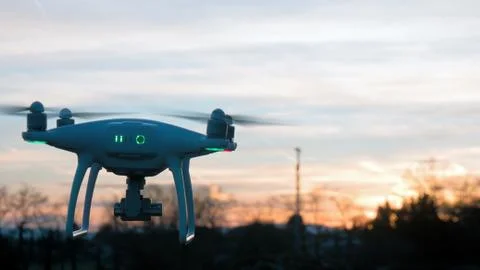 A drone hovers in flight in front of a sunset background Stock Photos