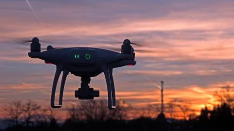 A drone hovers in flight in front of a sunset background. Stock Photos