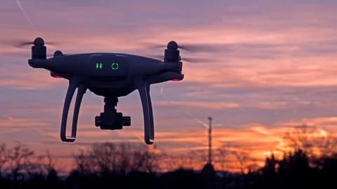 A drone hovers in flight in front of a sunset background. Stock Photos