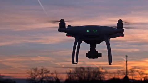 A drone hovers in flight in front of a sunset background. Stock Photos