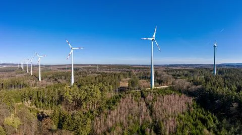 Drone image of a wind farm with towering wind turbines in a forest patch under Stock-Fotos