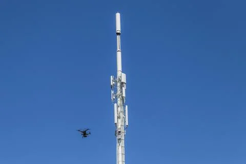 Drone inspecting a cell tower on the lower left Stock Photos
