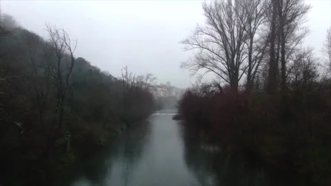 Drone low along river between trees to village Stockbeeldmateriaal 347585218