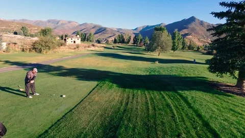 Drone low to tee off and pan rise to follow ball and see mountains Video stock 105605600