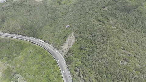 Drone lowers as camera pans up over coastal highway with paragliders above Stock Footage 326769807