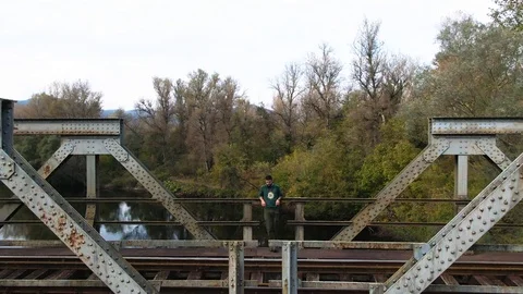 Drone man leaning on a bridge turning around to view nature's splendor Stock Footage 111157507