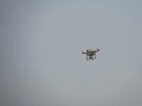 A drone in mid flight captured against a cloudy sky, stock photo. Stock Photos