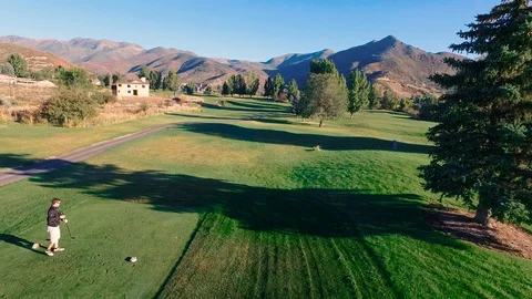 Drone mid height man tee off with mountains in back zoom in and out Stock Footage 105605563